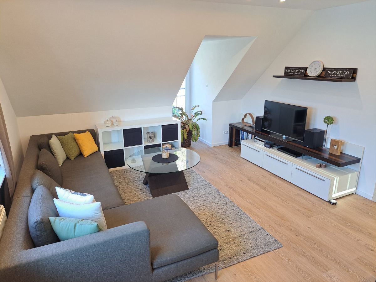 Renoviertes Wohnzimmer mit Ecksofa und Dachschräge